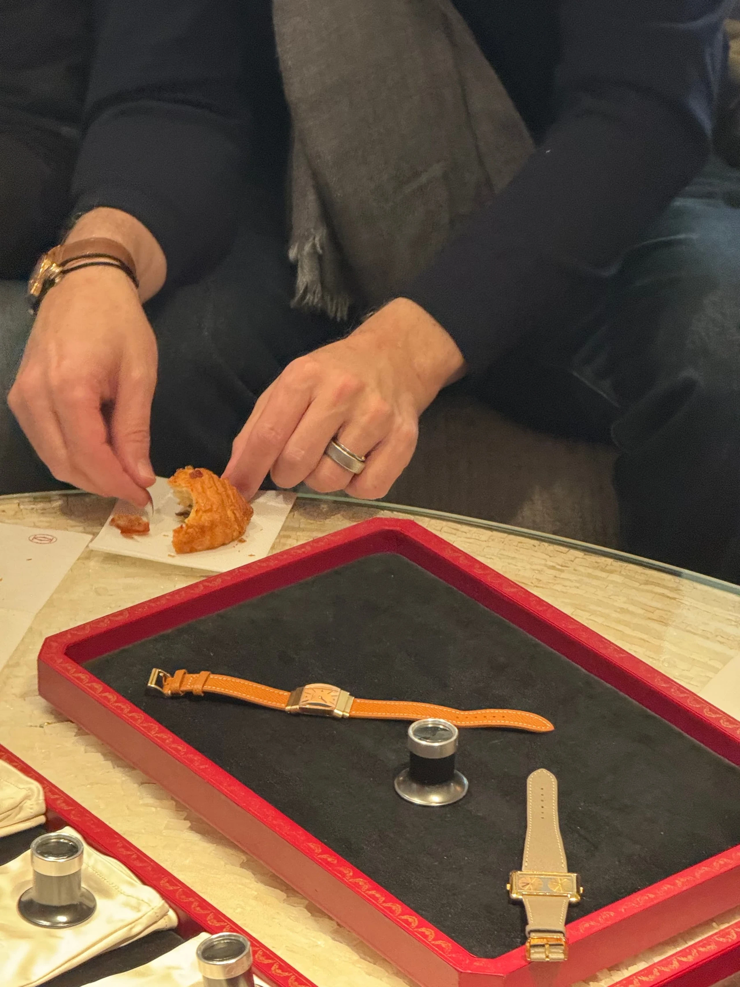 Hands handling vintage Cartier watches laid out on red trays